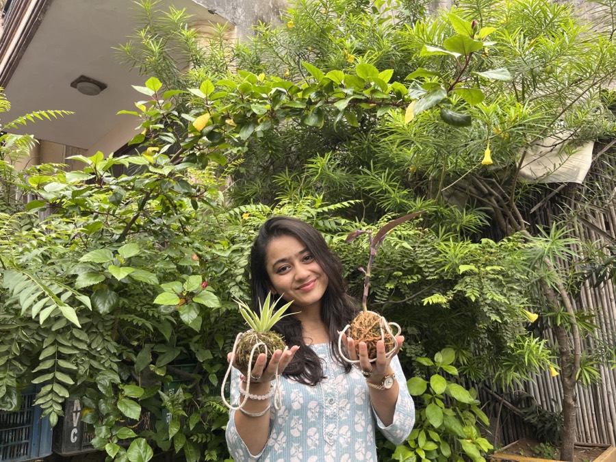 Chhavi Agarwal in dense foliage, holding two potted plants