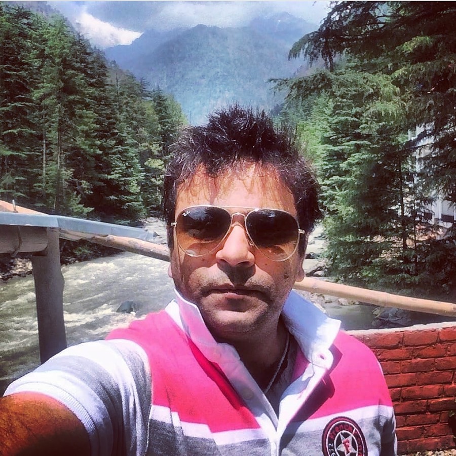Naveen Pabla in sunglasses, a river and pine slope behind him
