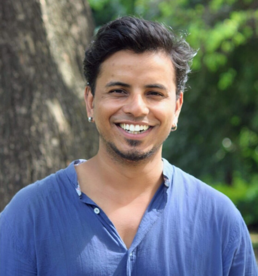 Nikhil smiling in front of a tree trunk