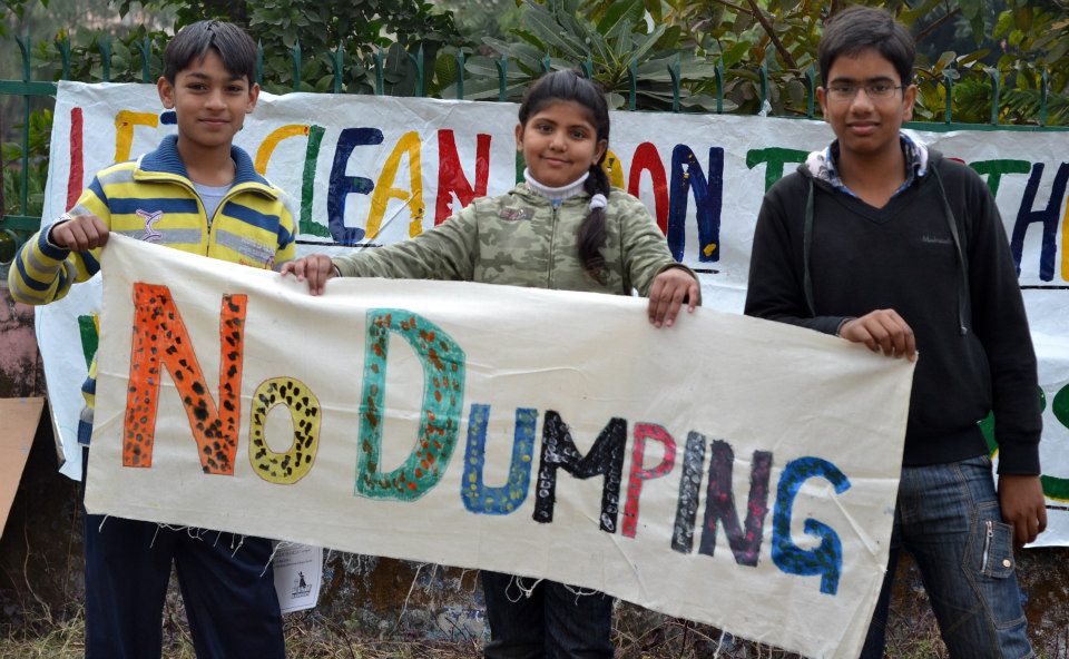 Three children holding up a hand-painted cloth banner reading No Dumping