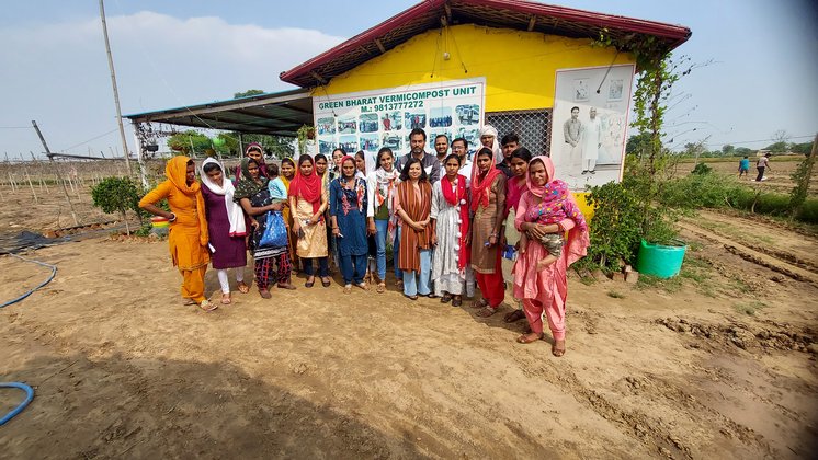A large group standing for a photograph outside a building signed Green Bharat Vermicompost Unit