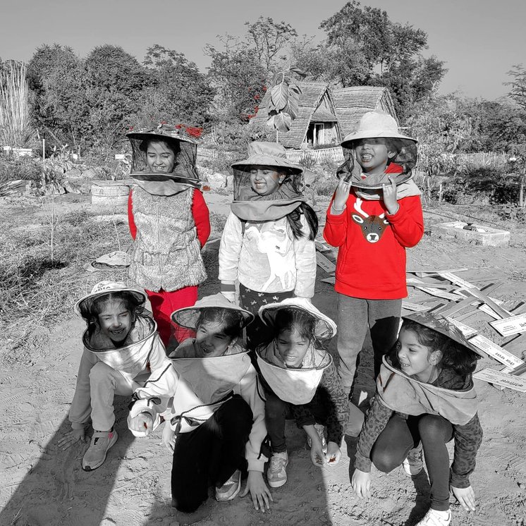 Children in beekeeping veils crouched together, grinning