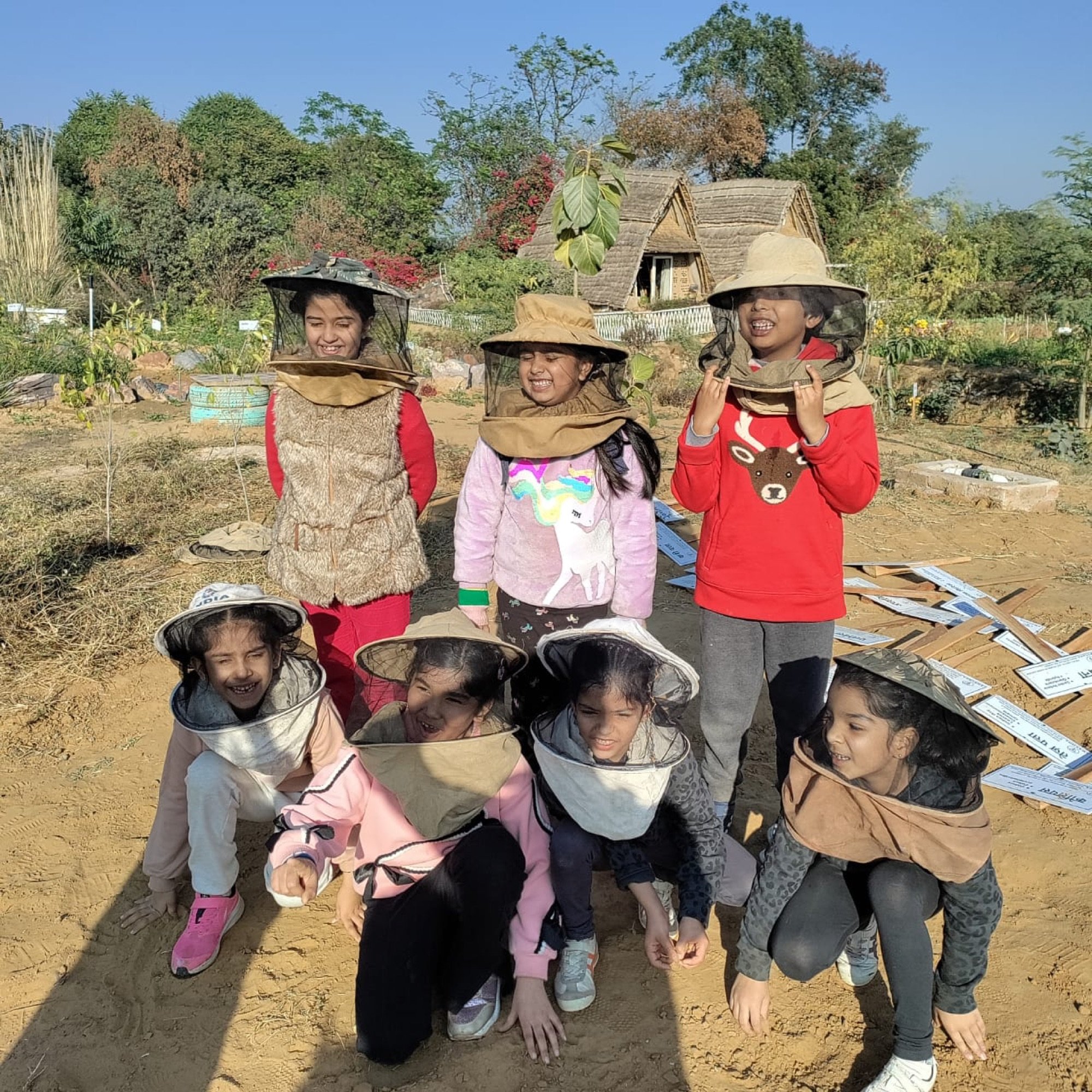 Children in sun hats and red jackets at a planting site