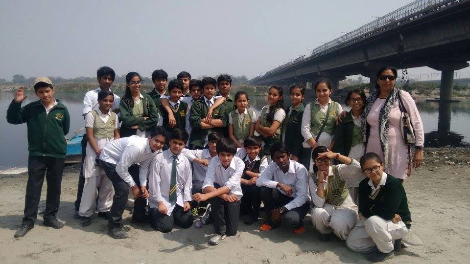 A school group in blazers posed for a photograph on a sandy Yamuna bank, a road bridge behind them