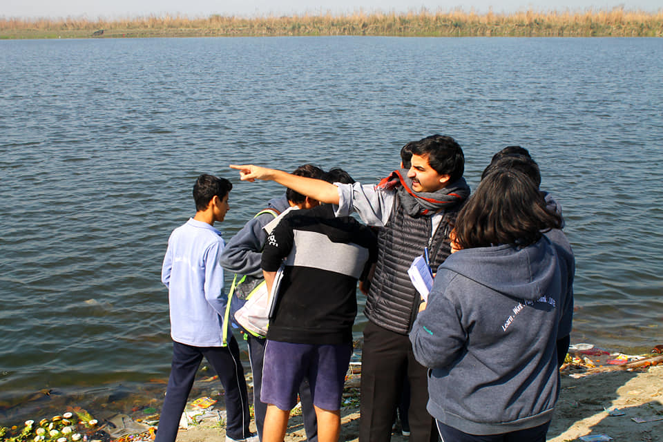 A facilitator pointing out across the Yamuna to a small group of students standing on the bank