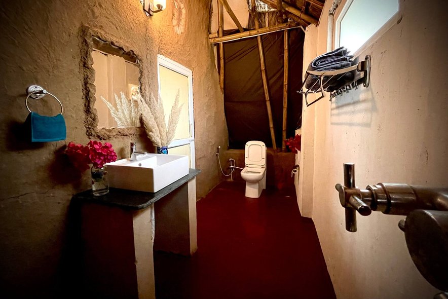 A washroom built into a mud wall, a basin and dried grass in the alcove
