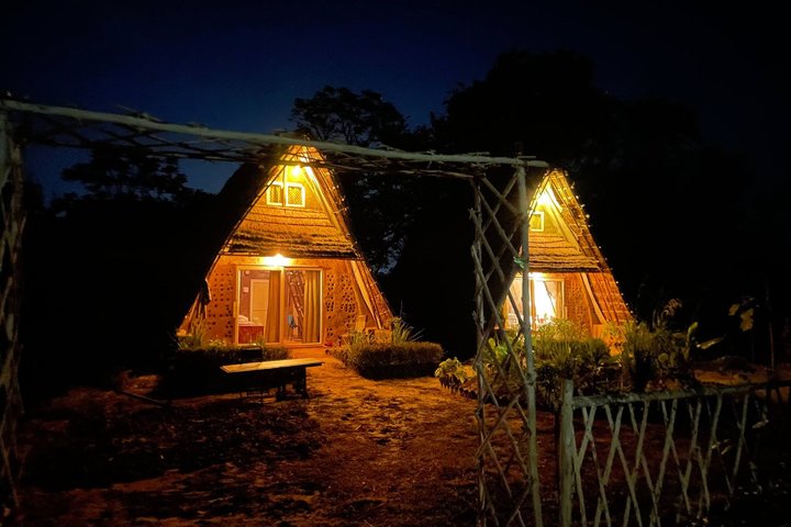 The mud houses lit from inside after dark, their windows warm against the field