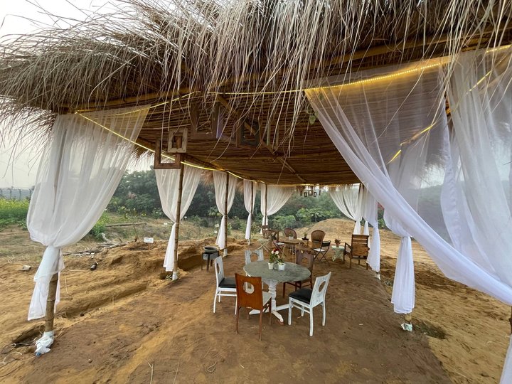 An open pavilion under thatch, drapes tied back around a round table and chairs