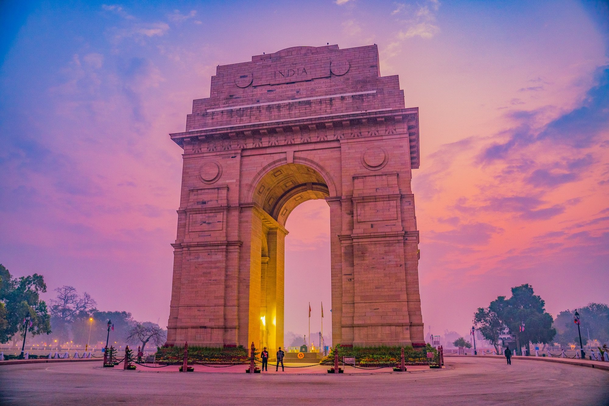 India Gate at dusk, its lamps lit under a hazy sky