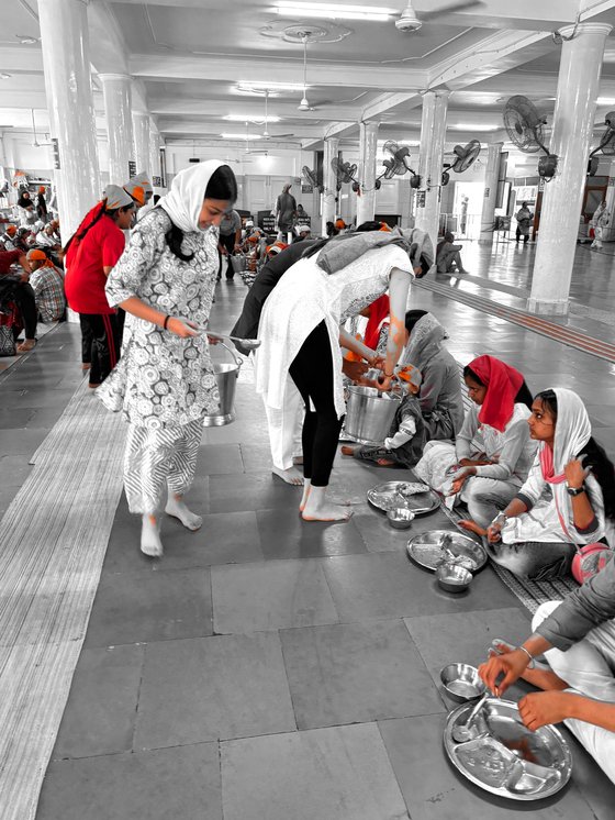Volunteers serving a shared meal down a seated line in a langar hall