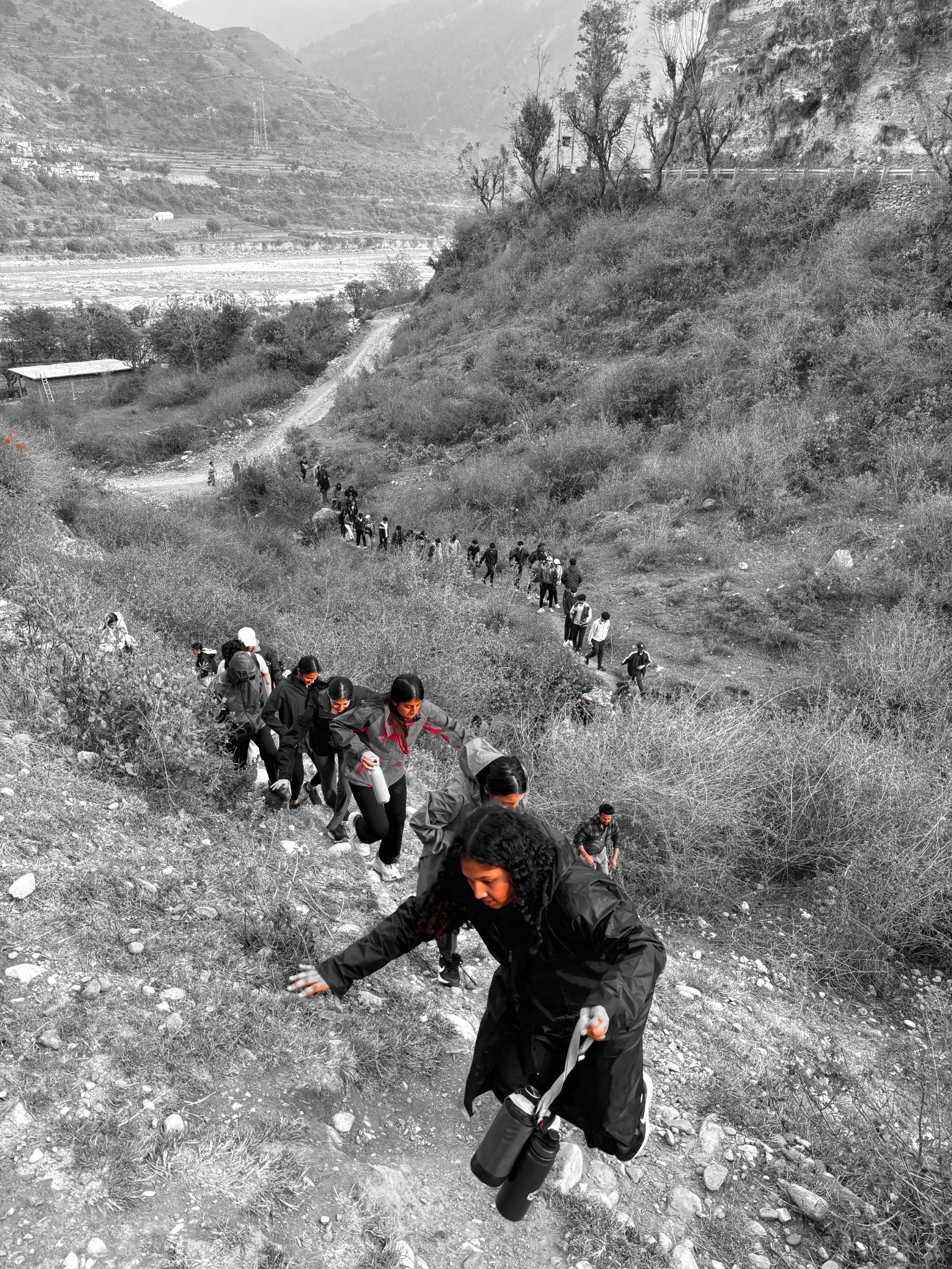 A long line of walkers climbing a hillside path above a river valley